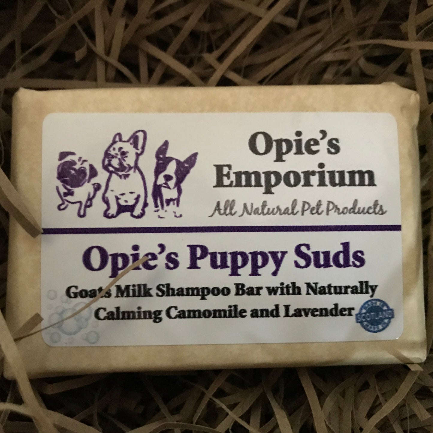 A bar of Opie's Emporium Puppy Suds goat's milk shampoo for pets, placed on a straw background.